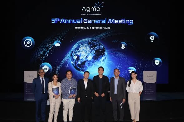 Seven people in business attire pose on stage in front of a large AGM backdrop with a glowing globe graphic