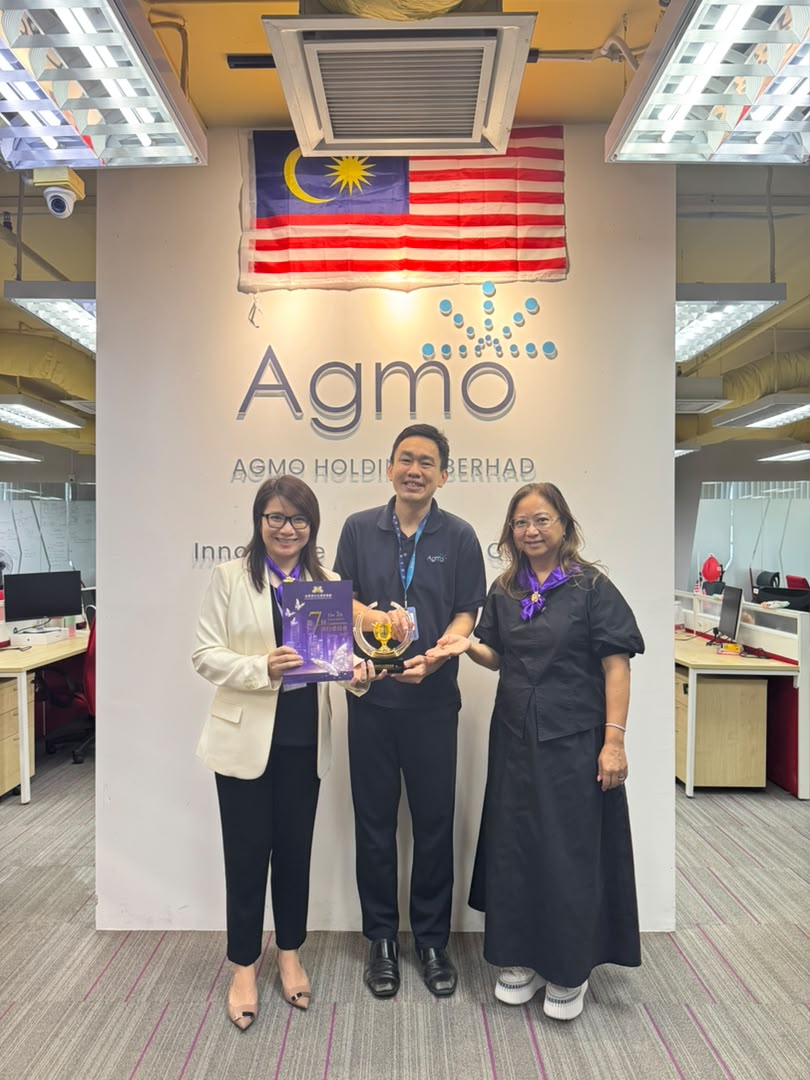 Two GBWEA delegates and an Agmo team member holding a commemorative plaque and award in front of the Agmo wall sign