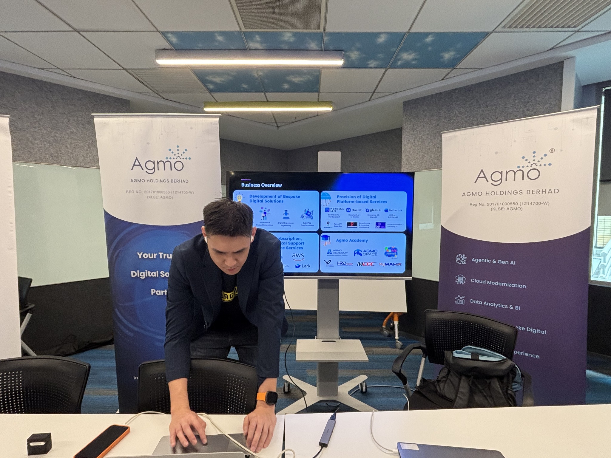An Agmo team member setting up a laptop in front of Agmo banners and a presentation screen