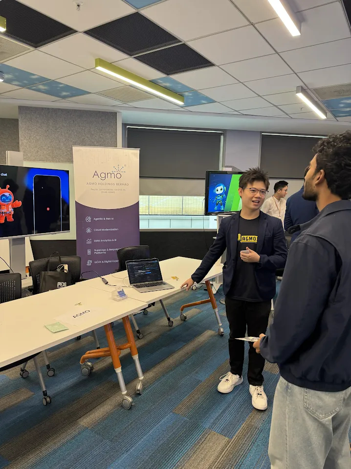 An Agmo speaker demonstrating an app to an attendee beside a laptop and screen